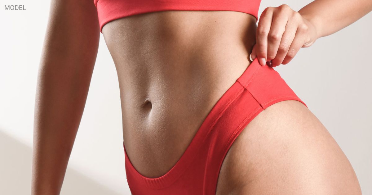 Close-up of a woman's flat stomach (model) wearing a red swimsuit against a white background.